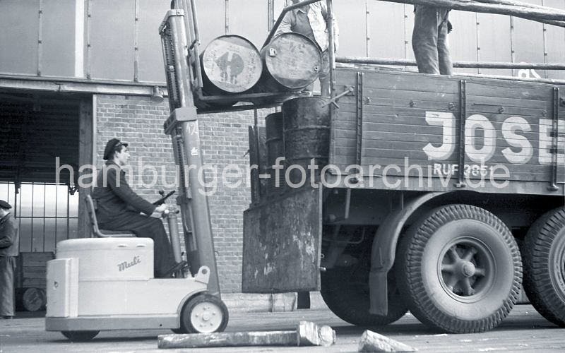 Fotos zur Geschichte des Hafen Hamburgs - Bilder aus dem Fotoarchiv der HHLA Gabelstapler Muli - Ladeflche Lastwagen / Sdwesthafen, Togokai; 1952.  521_0002 Der Fahrer des Gabelstaplers "Muli" hebt mit der Gabel des Flurfrdergerts zwei Tonnen auf die Ladeflche des Lastwagens am Togokai des Sdwesthafens. Zwei Arbeiter verladen die Tonnen auf dem Lastkraftwagen.