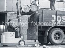 521_0002 Der Fahrer des Gabelstaplers "Muli" hebt mit der Gabel des Flurfrdergerts zwei Tonnen auf die Ladeflche des Lastwagens am Togokai des Sdwesthafens. Zwei Arbeiter verladen die Tonnen auf dem Lastkraftwagen. 