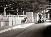 557_390a Ein Transportarbeiter fhrt seine Ladung mit dem Elektrokarren und ihren Anhngern in den Lagerschuppen des Hamburger Hafens. Dort sind unterschiedlich grosse Holz-Kisten gestapelt, die auf ihren Weitertransport warten.