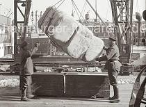 663_726 Die Ladung eines Frachters wird gelscht; der Hafenkran setzt drei Baumwollballen am Hafenkai ab. Die Kaiarbeiter nehmen die Hieve in Empfang - im Vordergrund wartet schon ein Arbeiter mit Sackkarre, um die Ware in den Kaischuppen zu transportieren.