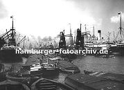 0953976 Blick in den  Hamburger Segelschiffhafen ca. 1930, links wird ein Frachtschiff am Americakai mit Krnen entladen - Motorschiffe und Lastkne liegen mit ihrer abgedeckten Ladung im Hafenbecken. In der Bildmitte entladen zwei Getreideheber einen Frachter und beladen lngsseits liegende Khne mit dem Getreide.