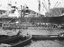 184_11 Das Frachtschiff DORA OLDENDORFF liegt in der Mitte des Roßhafens an den Dalben. Schuten mit Kisten an Bord haben längsseits fest gemacht. Im Vordergrund warten Ewerführer mit ihren Kähnen mit Hilfe des Schleppers auf ihren Arbeitseinsatz.