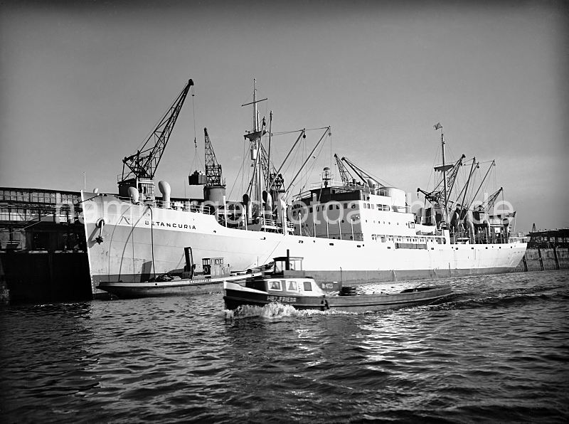 Bananenfrachter / Kühlfrachter, Segelschiffhafen - Asiakai   445_3 Der weisse Bananenfrachter BETANCURIA liegt am Asiakai im Segelschiffhafen, einem der vielen Hafenbecken des Hamburger Hafens. Ein Kran hievt gerade eine Ladung Bananen aus dem Laderaum des Kühlfrachters. Ein Wasserboot hat längsseits des Frachters festgemacht und pumpt über einen Schlauch Frischwasser an Bord. Die Barkasse FRIEDA fährt in voller Fahrt durch den Hafen.