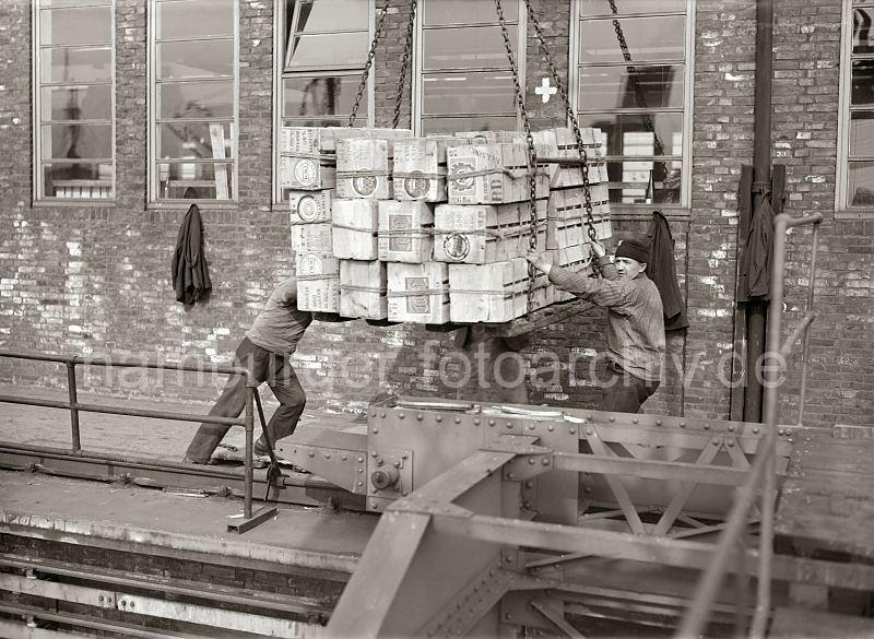 458_417 Ein Kranf�hrer setzt die Hieve Apfelsinenkisten auf der Galerie des Fruchtschuppens ab - Lagerarbeiter dirigieren die Ladung an ihren Platz; im Vordergrund das Schienensystem mit F�hrung des Halbportalkrans.�  Historische Arbeitsfotos aus dem Archiv der Hamburger Hafen und Logistik AG. Alte Bilder aus dem Hamburger Hafen - Hamburgmotive auf Fotoleinwand / Posterprint als Geschenk fuer Buero und Wohnung.