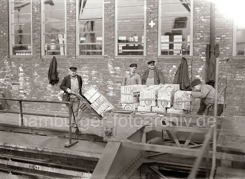 458_417a Die Hieve Apfelsinenkisten ist auf der Galerie des Fruchtschuppens abgesetzt - und das Ladegeschirr abgenommen. Von Hand werden die einzelnen Kisten aus der Partie auf die Sackkarre geladen und in den Fruchtschuppen transportiert.  Historische Arbeitsfotografien aus dem Bildarchiv der Hamburger Hafen und Logistik AG HHLA. Alte Hamburgmotive + Hamburgensien auf Fotoleinwand / Posterprint als Geschenk fuer Buero und Wohnung.