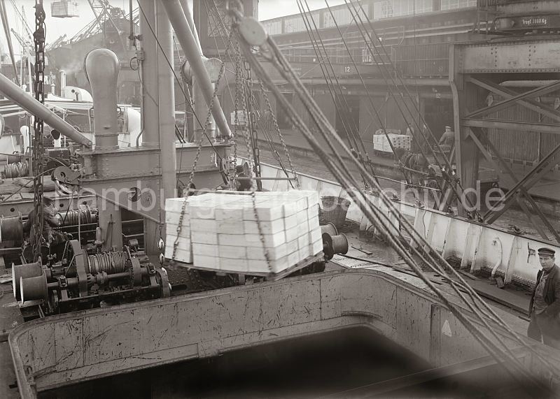historische Fotos von der Arbeit im Hamburger Hafen - Schiffsladung l�schen; ca. 1932. Alte Hafenbilder aus dem Fotoarchiv der Hamburger Hafen und Logistik AG. 470_576a Die Ladung Rosinenkisten wird aus der Ladeluke des Frachters gel�scht. An Land warten die Hafenarbeiter auf die Kisten, um diese im Fruchtschuppen zu stapeln. An der Laderampe stehen Pferd und Wagen und warten darauf beladen zu werden.�