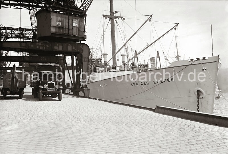Frachtschiff am Versmannkai des Baakenhafens - LKW unter Halbportalkran; Geschichte des Hamburger Hafens. 477_13_B_265 Der Fruchtfrachter AFRICAN REEFER hat am Versmannkai des Hamburger Bakenhafens vor dem Fruchtschuppen A fest gemacht. Unter dem Portalkran der Herstellerfirma KAMPNAGEL steht ein Lastkraftwagen mit Plane und Anhnger. Die Kaianlage ist mit Kopfsteinpflaster gepflastert.