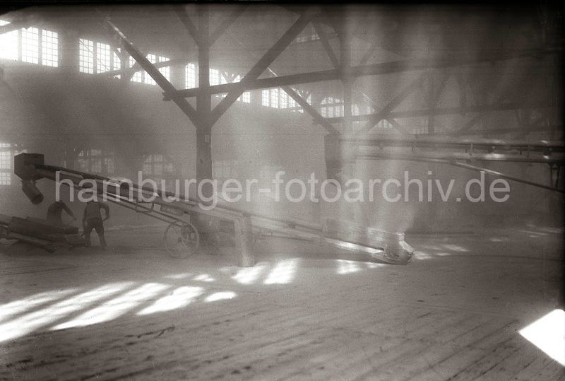 Alte Fotos aus dem Hafen Hamburgs - Fotos von der Geschichte des Hamburger Hafens; hamburger-fotoarchiv.de.Frderbnder im Hafenschuppen - Lagerarbeiter mit Schaufeln; ca. 1934  - 482_B_331a ber ein Frderband wird das Schttgut in den Hafenschuppen transportiert - dort fllt das Lagergut auf ein weiteres Transportband, um von dort zur Verteilung in den Raum gebracht zu werden. Zwei Lagerarbeiter arbeiten mit Schaufel im staubigen Raum.