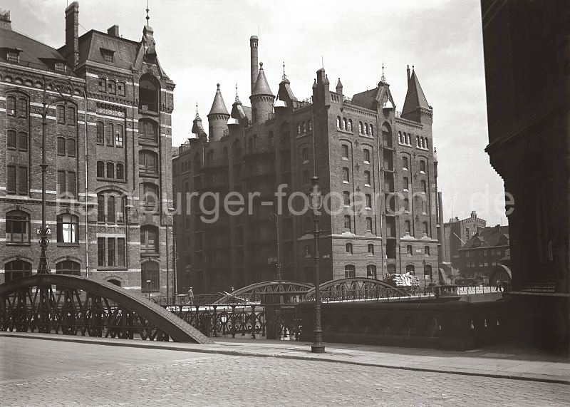 historische Backsteinarchitektur der Speicherstadt - Lagergebude im Hamburger Feihafen.  501_567 Blick vom Neuen Wandrahm zur Kannengiesserortbrcke und die Kaispeicher P (lks.) und Q (re.) Ein Pferdefuhrwerk fhrt mit Scken und Kisten hochbeladen auf der Kopfsteinpflaster-Strasse. Im Hintergrund rechts die Neuerwegsbrcke und die Fassade und der hohe Schornstein vom Kaispeicher B am Brooktorhafen.