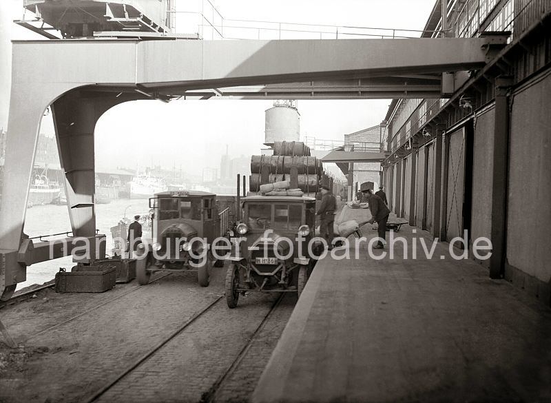 Alte Hamburgmotive aus dem Hafen - Fotoarchiv der HHLA -Gterumschlag am Sandtorhafen Hafenbahn und Lastwagen am Kaiserkai; ca. 1930.  513_431 Lastwagen werden an der Rampe des Lagerschuppens am Kaiserkai beladen - ein Hafenarbeiter schiebt eine Sackkarre mit Scken an die Ladeflche des LKW ein anderer Arbeiter ldt das Sackgut auf. Ein weiterer Lastkraftwagen wartet neben einem mit Metallfssern hoch beladenen Gterwaggon der Hafenbahn. Im Hintergrund sind die Frachtschiffe am Sandtorkai und der Kaispeicher B zu erkennen.