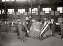 519_422 Von Hand setzen die Lagerarbeiter ein schweres Holzfass auf eine Transportkarre. Im Lagerraum des Hamburger Kaischuppens sind Tonnen und Säcke gelagert. 