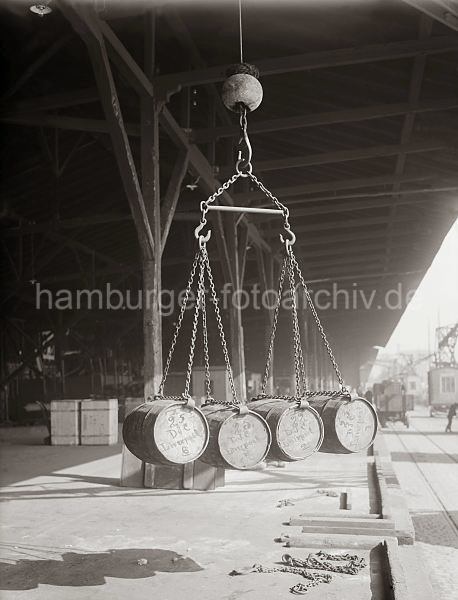 Historisches Fotomaterial vom Hafen Hamburg / Archiv HHLA Gterumschlag - Verladung von Fssern, Ladegeschirr; ca. 1930. 524_435 Vier Fsser hngen im Ladegeschirr des Hafenkrans ber der Laderampe des Lagerschuppens. Im Hintergrund steht ein Lastwagen an der Rampe.