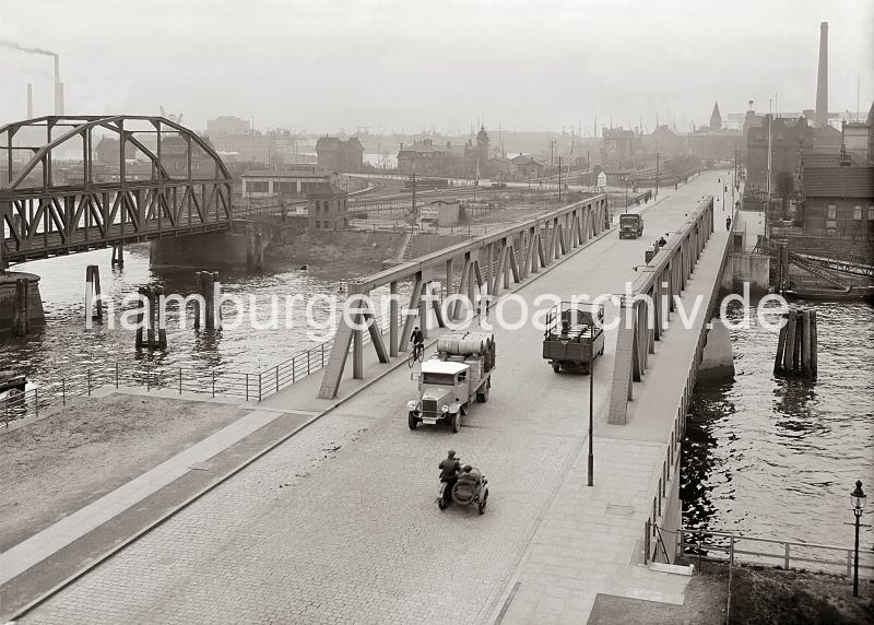 Bilder aus dem historischen Hamburger Hafen / Fotoarchiv der HHLA / Lastwagenverkehr auf der Reiherdamm Brcke, Reiherstieg - Ellerholzschleuse ca. 1930.  532_743a Blick ber den Reiherstieg vom Kleinen Grasbrook nach Steinwerder; mit Fssern beladene Lastwagen, Fahrradfahrer und ein Motorrad mit Beiwagen berqueren die Reiherdammbrcke. Links die Eisenbahnbrcke ber den Reiherstieg, dahinter Gebude der Ellerholzschleuse, die in den Oderhafen und Travehafen fhrt. Ganz lks. Schornsteine des HEW Elektrizitts-Werks an der Nippoldstrasse.