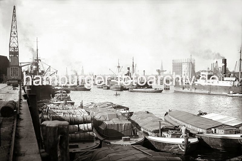 Alte Hamburgbilder aus dem Hafen / Lastkhne am Amerika Kai im Hamburger Segelschiffhafen - Frachter an Dalben  - Hamburger Gaswerke am Grasbrook; ca. 1934. 534_B_321a Die Lastkhne im Segelschiffhafen sind hoch beladen - bei den meisten ist die Ladung mit Planen gegen die Witterung abgedeckt -  andere Schuten haben eine Holzabdeckung fr ihren Laderaum. An den Dalben in der Mitte des Hafenbeckens werden Frachter ber Schuten be- und entladen. Im Hintergrund ist die Silhouette Hamburgers zu erkennen: in der linken Bildmitte der Turm der St. Michaeliskirche, dem Michel als Hamburger Wahrzeichen - auf der rechten Seite der Kirchturm der St. Nikolaikirceh und das Gasometer der Hamburger Gaswerke auf dem Grasbrook. Links davon ist der grosse Kran am Ende des Asia Kais auf Kranhft zu sehen.