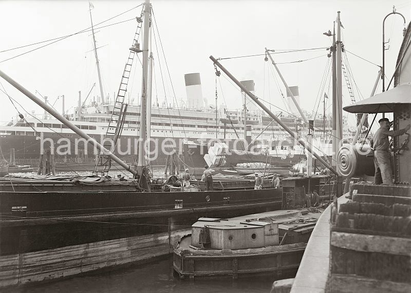 Historische Hafenbilder aus Hamburg / Bildarchiv der HHLA -- Motorschiff + Arbeitsschute am Johannisbollwerk - Passagierschiff Cap Arcona. 538_573 ber den Ladebaum einer Arbeitsschute wird eine Ladung Kisten vom Motorschiff an den Vorsetzen gelscht. Schauerleute stehen an der geffneten Luke des Laderaums und sichern den Vorgang der Entladung des Schiffs. Rechts steht ein Kranfhrer am stationren Kran auf der Kaianlage - im Hintergrund das Passagierschiff Cap Arcona.