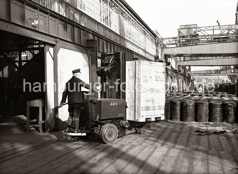 Historische Hamburgmotive aus dem Hafen / Hamburgfotos auf Leinwand - Geschenke zu Weihnachten oder Geburtstag. Elektrohubwagen der Firma AEG - Transportkiste und Fsser, Schuppen 83 - Chilekai, Oderhafen; ca. 1934.  546_143 Ein Lagerarbeiter hat eine groe Holzkiste auf die Gabel des Elektrohubwagen geladen und fhrt sein Transportgut auf die Lagerrampe des Schuppens 83 am Chilekai des Oderhafens. Auf der Rampe stehen Metallfsser, im Hintergrund ein Arbeiter mit einer Sackkarre.