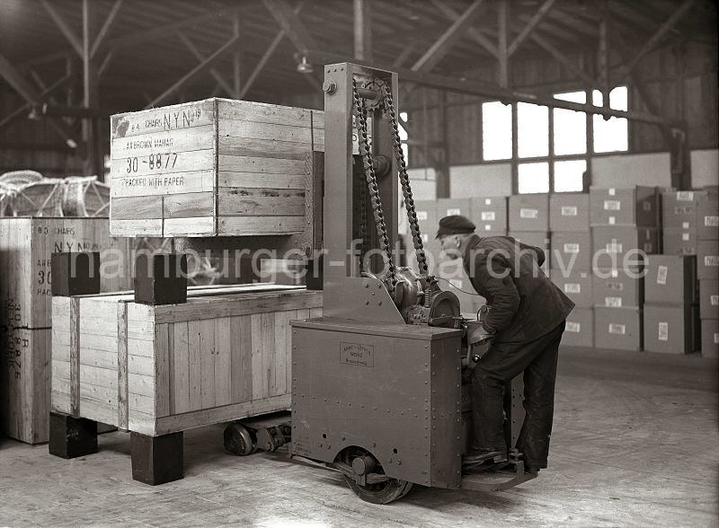 Alte Hamburgfotografien aus dem Hafen. Hamburgbilder als Geschenk zum Geburtstag + Jubilaeum - Elektrohubwagen der Firma Amme Luther - Lagerung von Holzkisten im Hamburger  Hafens ; ca. 1934.  548_186b Ein Fahrer des Elektrohubwagens der Herstellerfirma Amme Luther stapelt zwei Holzkisten bereinander. Die Kisten stehen auf Blcken als Abstandshalter, damit die Gabel und Vorderrder des Transportwagens Platz haben.