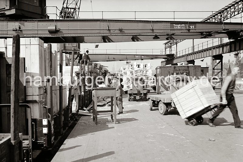 istorische  Hamburgfotos vom Hafen. Hamburgfotos als Geschenk zum Abschied, Buero. Entladen  eines Gterzuges - Hafenarbeiter mit Sackkarre +  Elektrotansportwagen; ca. 1934.  549_391 Ein Gterzug wird an der Laderampe entladen, er hat Sthle und Kisten geladen. Ein Arbeiter transportiert eine grosse Holzkiste mit einer Sackkarre, ein anderer Hafenarbeiter fhrt gerade mit der Karre die Laderampe auf den Gterwaggon hoch. Im Hintergrund ein Elektrokarren, der Sthle aufgeladen hat.