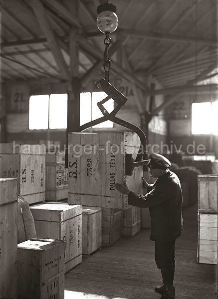 Alte Hamburger Hafenfotografien / Bildarchiv der HHLA. Holzkiste am Kistengreifer. Hamburgbilder als Weihnachtsgeschenk. 562_59 Eine Transportkiste hngt am Kistengreifer des Schuppenkrans; ein Lagerarbeiter dirigiert die Holzkiste an ihren Lagerplatz im Hafenschuppen.