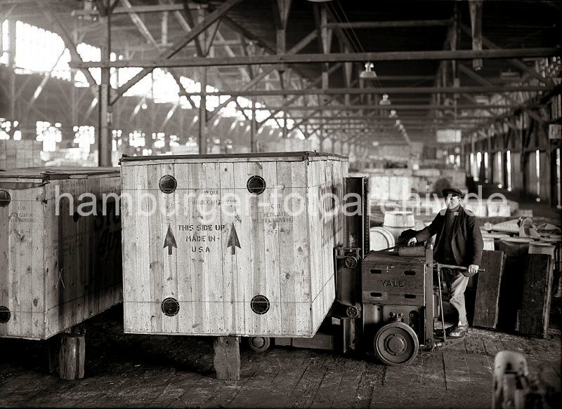 Bilder von der Geschichte der Arbeit im Hafen - Fotoarchiv HHLA. Elektrischer Hubwagen YALE - Holzkiste im Lagerschuppen im Hafen Hamburgs. 573_70 Eine grosse Holzkiste mit der Aufschrift Made in USA wird von einem Lagerarbeiter mit einem Hubwagen der Herstellerfirma YALE an ihrem Platz im Lagerschuppen abgestellt.