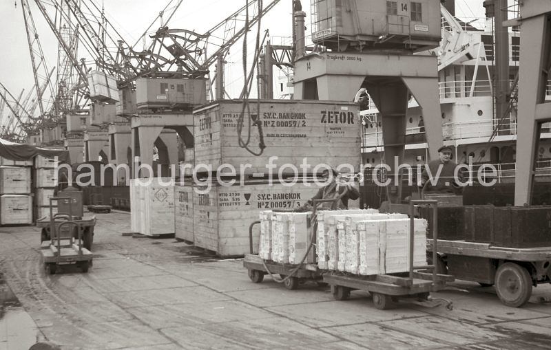 Bilder von der Geschichte der Technik im Hafen. Beladung eines Frachters im Kaiser-Wilhelm-Hafen/Kronprinzkai; Elektrokarren mit Anh�nger. 575_3 Ein Frachter wird am Kronprinzkai des Kaiser-Wilhelm-Hafens beladen. Dicht an dicht stehen die Hafenkrane der Herstellerfirma Kampnagel am Kai und hieven die Ladung an Bord des Schiffs; lks. schweben Holzkisten �ber dem Fahrer des Elektrokarrens - in der Bildmitte wird gerade das Tau, mit dem eine Ladung an Bord gebracht wurde wieder herabgelassen. Ein Hafenarbeiter macht gerade eine Hieve, die auf Anh�ngern der Elektrokarren liegt, fertig, damit sie an Bord des Frachtschiffs gebracht werden kann.