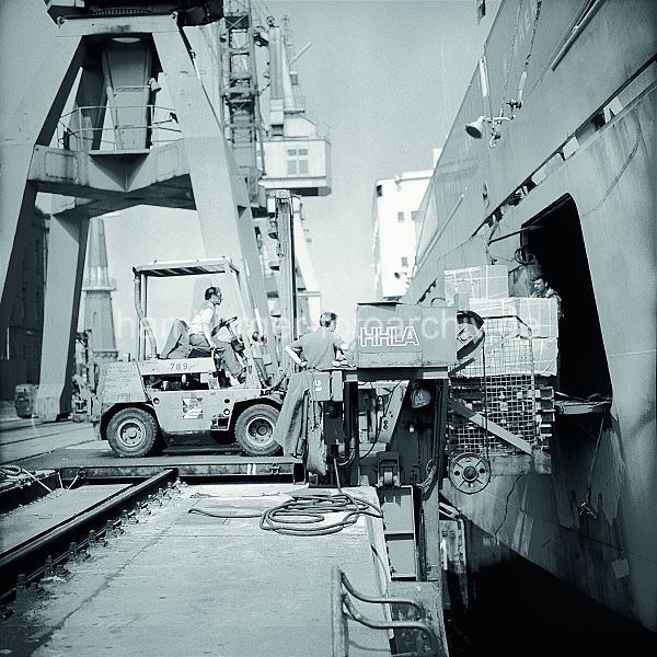 Geschichte der Arbeitstechnik im Hamburger Hafen Bilder aus dem Fotoarchiv der HHLA - Gabelstapler der HHLA bel�dt einen Frachter; ca. 1972.  577_03 Der Fahrer eines Gabelstaplers f�hrt auf die Laderampe auf dem Kai und schiebt eine Palette mit Kisten durch eine Luke in der Seitenwand des Frachters.�