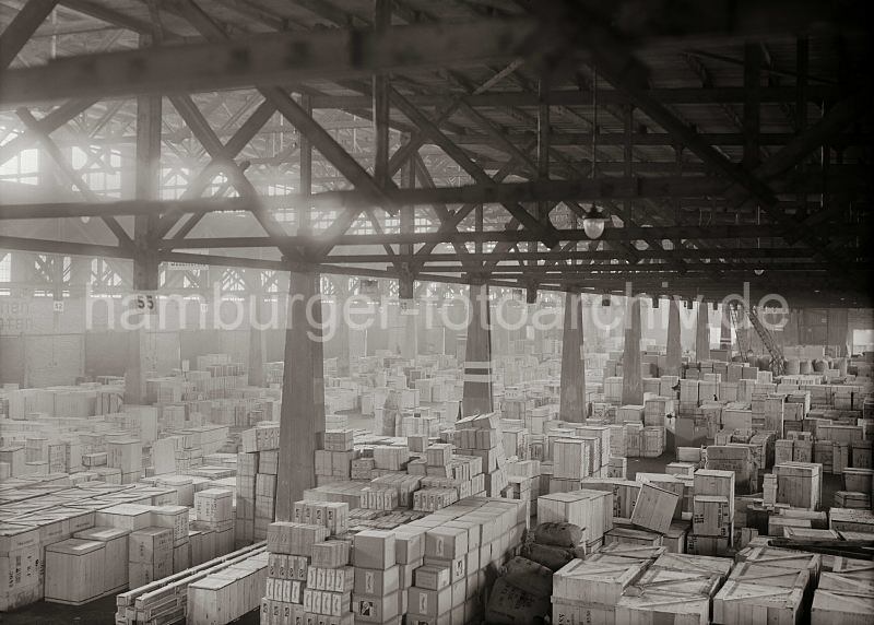 Geschichte des Hafens; Bilder aus dem Fotoarchiv der Hamburger Hafen und Logistik AG, HHLA - Lagerschuppen am Sdwesthafen / Indiahafen - Verteilungsschuppen, Kistenlagerung; ca. 1931.  578_641 Kaischuppen / Verteilungsschuppen 57/58 am Indiahafen; die einzelnen Lagerpartien sind nach Bestimmungsort gelagert. Durch die Fenster unter der Decken des hohen Gebudes fllt gleichmssig Licht in den Lagerraum - fr den Nachtbetrieb sind Lampen in den Gngen installiert. Im Hintergrund arbeitet rechts ein fahrbarer Schuppenkran zwischen den Kistenstapeln.