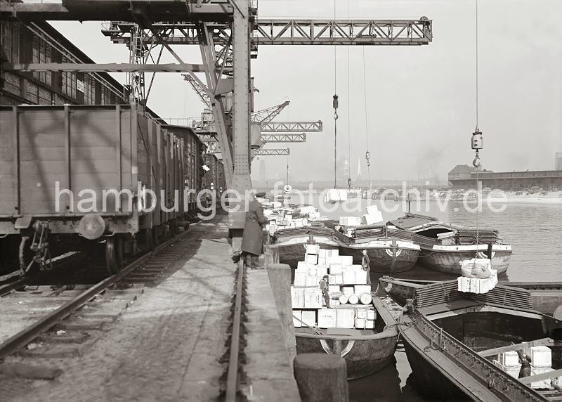 historische Hamburgfotos aus dem Archiv der Hamburger Hafen und Logistik AG HHLA. Schuten am Afrikakai des Sdwesthafens - beladene Lastkhne; Gterumschlag im Hafen Hamburgs.  580_645a Die Schuten liegen dicht gedrngt am Afrikakai des Sdwesthafens - die Lastkhne haben keinen eigenen Antrieb sondern werden mit Schleppern ber das Wasser des Hamburger Hafens bewegt. An den Kranhaken der Kaikrane hngen Kisten, die auf die Transportschiffe verladen werden. Im Hintergrund sind die Kirchtrme Hamburgs auf der anderen Seite der Elbe zu erkennen; ganz rechts ein schmaler Anschnitt des Gasometers der Gaswerke auf dem Groen Grasbrook.
