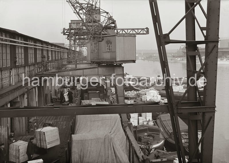 Historische Hamburgbilder aus dem Fotoarchiv der HHLA. Halbportalkran am S�dwesthafens - Gueterumschlag im Hafen der Hansestadt Hamburg. 581_646 Blick von einem Halbportalkran auf den G�terumschlag im Hamburger Hafen - gro�e Kisten werden �ber die an der Laderampe stehenden G�terwaggons verladen. An der Kaimauer vom Hafenbecken des S�dwesthafens liegen mit G�ter beladene Schuten.