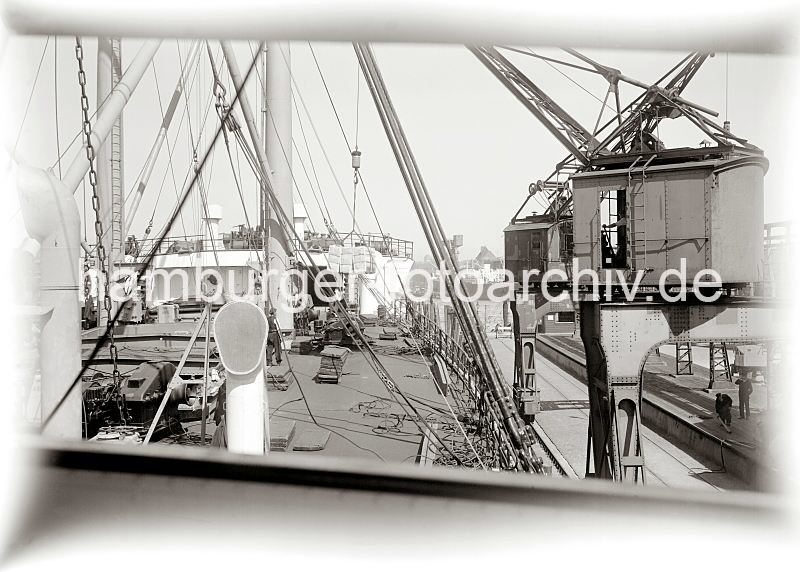 Historische Hafenbilder aus dem Fotoarchiv der Hamburger Hafen und Logistik AG. Die Ladung eines Frachter wird am Australiakai des Indiahafens gel�scht - Hieve Kisten am Kranhaken.  583_660a �ber die Halbportalkrane auf der Kainanlage des Asiakais im Indiahafen wird die Ladung eines Frachtschiffs gel�scht. Eine Hieve Kisten h�ngt am Kranhaken und wird an Land gebracht, wo Arbeiter auf der Laderampe darauf warten, in Empfang zu nehmen.