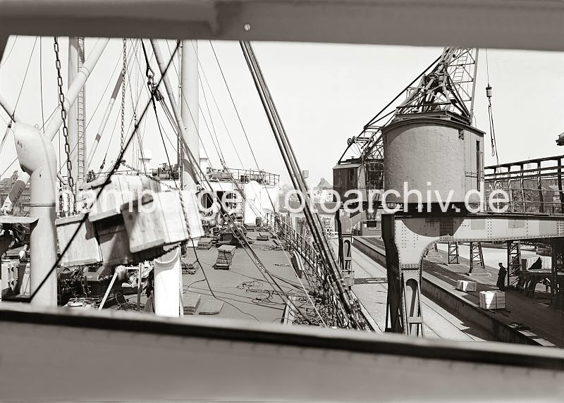 Historische Hafenbilder aus der Hansestadt Hamburg. Ladung l�schen eines Frachtschiffs im Hamburger Hafen / Indiahafen, Australiakai - Kisten am Kranhaken.  584_661 Arbeit im Hafen der Hansestadt Hamburg; ein Frachtschiffs wird entladen - Holzkisten h�ngen von einer Eisenkette zusammengehalten an dem Kranhaken und werden an Land gebracht. Auf der Laderampe des Hafenkais stehen schon abgeladene Kisten, die auf ihren Weitertransport in den Lagerschuppen warten.