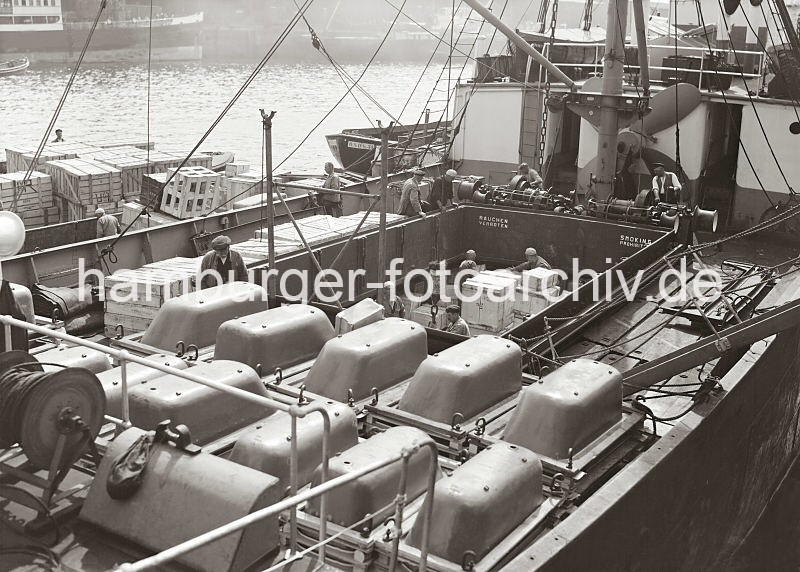 Hafenmotive von der Hansestadt Hamburg - Bildarchiv der HHLA: Ladung eines Frachters im Grasbrookhafen, Laderaum mit Kisten; ca. 1936.  605_669a Blick auf einen Frachter am Dalmannkai des Grasbrookhafens. An Deck des Frachtschiffs sind Badewannen gestapelt - aus dem Laderaum werden groe Holzkisten mit dem Kran herausgehoben. Im Hafenbecken liegen mit Kisten beladene Schuten lngsseits.