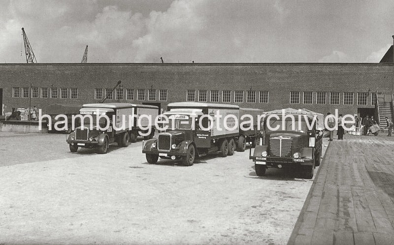 Bild-Dokumentation der Geschichte des Hamburger Hafens - Fotoarchiv der HHLA. Lastwagen mit Anhnger am Verteilungsschuppen 57, Kamerunkai / Indiahafen; ca. 1936. 613_3502_59 Mehrere Lastkraftwagen mit Anhnger stehen an den Laderampen des Verteilungschuppens 57 am Kamerunkai des Indiahafens. Die Ladeflache des LKW ist ebenso wie dessen Anhnger mit einer Plane geschtzt, auf seiner Stossstange steht die Bezeichnung " Bsing Diesel". Im Hintergrund transportieren Arbeiter Kisten mit der Sackkarre in den Lagerschuppen.