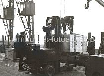 630_03502_30 Mit Hilfe eines Hubwagens wurde die große Holzkiste aus dem Lagerschuppen auf den Hafenkai gefahren. Dort bereiten zwei Hafenarbeiter die Kiste für die Verladung vor. Auf der Stirnseite der Kiste ist u.a. die Bezeichnung "Made in Germany" und der Bestimmungsort "New York" gedruckt.