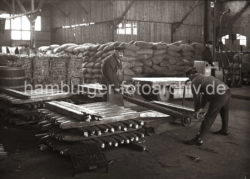 Beladen des Anh�ngers eines Elektroschleppers mit Kupperbarren; ca. 1932 634_53 Von einem Stapel Kupferbarren haben zwei Arbeiter mit Handhaken einen der Metallbarren aufgenommen und legen diesen auf den Anh�nger eines Elektrokarrens. Im Hintergrund steht der Fahrer des Elektroschleppers auf seinem F�hrerstand, einer der Anh�nger ist schon beladen.