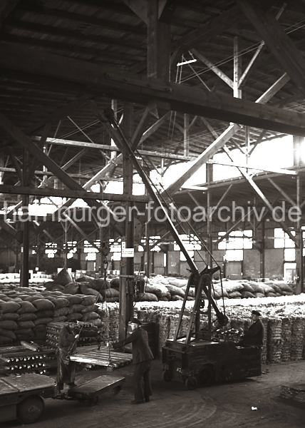 Ein Laufkran transportiert Kupferbarren im Hafenschppen; ca. 1932.  636_56 Mit einem Elektrolaufkran wird eine Partie Kupferbarren auf en Anh�nger eines Elektroschleppers geladen. in dem Hafenlager sind S�cke und Baumwollballen gestapelt.