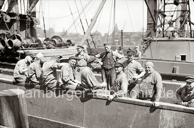 Schauerleute an Bord eines Frachters machen Pause; ca. 1934. 640_0228 Pause der Arbeiter auf einem Frachter - die Hafenarbeiter sitzen in der Sonne, einige rauchen, einer hat eine Flasche Bier in der Hand. Die meisten der M�nner tragen einen "Elbsegler", die typische Hamburger Schirmm�tze mit Kordel. Die Aufgabe der sogen. Schauerleute besteht im Stauen bzw. dem Be- und Entladen der Frachschiffe. Der Begriff Schauermann stammt vom niederl�ndischen Wort sjouwen = schleppen. Die Arbeiter im Hafen Hamburgs waren zumeist Tagel�hner, die zur Erledigung einer konkreten Arbeit eingestellt wurden.