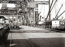 652_543b Auf der Gleisanlagen der Hafenbahn stehen Güter- waggons vor der Laderampe; Kaiarbeiter sind dabei die Ladung des Güterzugs auf Transportkarren zu stapeln. Rechts die Decksauf- bauten eines Frachter an der Kaimauer des Oderhafens. 