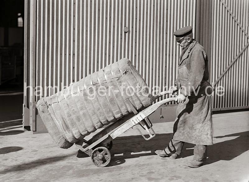 Bildmaterial zur GEschichte des Hamburger Hafens - Handarbeit im Hafen - Transport eines Ballen mit der Sackkarre; ca. 1934.  674_309_421 Der Kaiarbeiter m transportiert einen Ballen, der mit Bandeisen zusammengehalten wird auf seiner Sackkarre. Der Hafenarbeiter trgt seine Dienstmtze und eine Schrze zum Schutz seiner Kleidung.