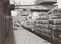 697_654 Ein Güterzug wird mit dem Rohstoff Kork im Hamburger Hafen beladen; die Rinde der Korkeiche wird hoch auf den offenen Güterwaggons an der Rampe gestapelt. Ein Kaiarbeiter fährt eine Sackkarre mit einer Fuhre Kork an den Waggon heran während zwei Hafenarbeiter eine Hieve des Krans entgegen nehmen.