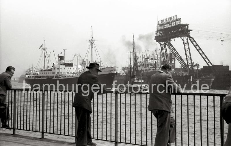 Hafen-Bilder der Nachkriegszeit Hamburgs -Schaulustige auf den St. Pauli Landungsbrcken - Stlckenwerft, 1956. 722_3 Schaulustige stehen auf den Landungsbrcken und sehen dem Schiffsverkehr auf der Elbe zu - der Frachter SANTA CATRARINA wird von dem Schlepper W. TH. STRATMANN aus dem Hamburger Hafen geschleppt. Im Dock der Stlckenwerft liegt ein Schiff zur Reparatur - an dem Portal der Kabelkrananlage ist der Schriftzug der 1840 gegrndeten Hamburger Werft angebracht.