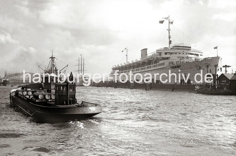 Hamburgensien als Geschenk fr Jubilaeum in der Firma / Bro, Transportschiff mit lfssern - Passagierschiff WILHELM GUSTLOFF; 1938.  733_364a Im Vordergrund transportiert ein Hafenfahrzeug der Deutschen Vacuum Oel AG Fsser. Die WILHELM GUSTLOFF hat am Anleger fest gemacht - Arbeiter hngen auf Plattformen vor dem Bug des Schiff und streichen die Bordwand.