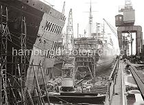 758_631 Schwimmdock der 1877 gegründeten Werft Blohm & Voss - Werftkräne stehen am Rand des Docks und transportieren Arbeitsmaterial zum Schiff. Im Vordergrund liegen ein Schwimmkran und eine Arbeitsschute an der Stirnseite der Dockanlage.