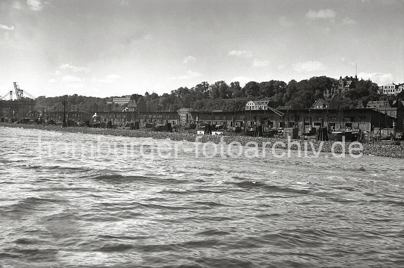 Alte Fotografien Altona - Fischereihafen Hamburg-Altona, Elbhang Wohnhuser; ca. 1937. AltonaBilder als Kunstdruck auf Leinwand + Poster. 807_B_220a Blick ber das Wasser der Elbe zum Fischereihafen Altona; ein Damm schtzt die am Kai liegenden Schiffe vor dem Schwall und Wellengang vorbeifahrender Schiffe. Hinter den Kaischuppen, auf deren Laderampen Fischkisten gestapelt sind, liegt der Elbhang mit Wohngebuden. Links im Hintergrund Krne des Altonaer Kohlehafens.