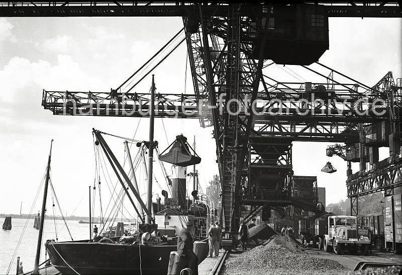 Alte Aufnahmen Altonas - Lschung der Kohleladung eines Frachters - Schttgut am Hafenkai; Krananlagen im Kohlehafen Altona; 1938. Altonaer Bilder auf FotoleinwandLeinwand + als Fotoposter. 815_B_289 Die Ladung eines Kohlefrachters wird am Kai des Kohlehafens in Altona gelscht. ber die Ausleger der Krananlage werden die Greifer in den Laderaum des Schiffs herabgelassen. An Land wird das Schttgut ber Frderbnder auf Halde gelagert oder gleich in Gterwagen oder Lastkraftfahrtzeuge verladen. Eine Zugmaschine mit zwei voll beladenen Anhngern steht an der Verladestation.