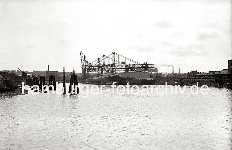 Alte Harburger Fotografien - Kohlenfrachter am Kai, Kohlekrne und Schuten, Binnenschiffe; ca. 1938 - historische Harbugfotos als Geschenk zum Geburtstag, Jubilaeum + Weihnachten. 822_B_258 Im Seehafen wird die Fracht eines Kohlenfrachters gelscht - ein Elbkahn liegt lngsseits, der Laderaum ist aufgedeckt. Hinter den Holzdalben sind die Halbportalkrne am Kai zu erkennen - dort liegen Schuten und Frachtkhne in mehrere Reihen. An der Stirnseite des Hafenbeckens befinden sich Industriegebude und Lagerhuser