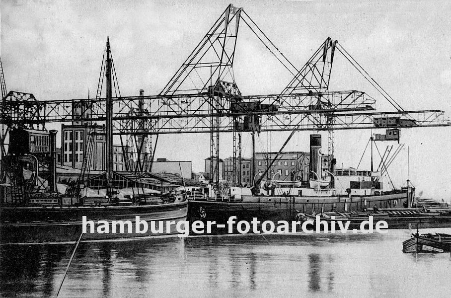 k_0954022 Frachtschiffe liegen im Harburger Seehafen am Kai - die Kranausleger sind heruntergelassen und beladen oder entladen die Schiffe. Eine Schute liegt am Dampfschiff längsseits und wird mit bordeigenem Ladebaum  geladen; im Hintergrund Harburger Fabrikgebäude.