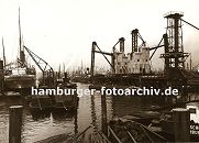 k_119690 alte Bilder aus Hamburg : Blick in den Kuhwärder Hafen - dicht gedrängt liegen die Schiffe in dem Hamburger Hafenbecken; rechts die stationäre pneumatische Anlage, um das Schüttgut wie z.B. Getreide aus den Frachtschiffen zu löschen. Im Vordergrund Duckdalben, die aus Nadelholz-Baumstämmen angfertigt sind und tief in den Hafengrund getrieben, den Schiffen zum anlegen oder festmachen dienen. Das Ende dieser dicken Pfähle ist mit Metall belegt, damit kein Wasser in die Stirnseite der Stämme dringen kann.