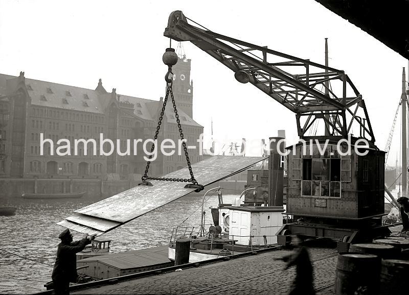 Bilder aus dem historischen Hamburger Hafen - Arbeit am im Sandtorhafen / Sandtorkai, Hafenkran; ca.1934. 01175_63 Am Sandotorkai des Sandtorhafens werden Blechplatten mit einem Hafenkran verladen - mit einem speziellen Anschlag hebt der Kran die Fracht in die H�he, um sie auf das am Kai liegende Schiff zu verladen. Ein Hafenarbeiter dirigiert die Fracht mit den blossen H�nden. Im Hintergrund die Seitenansicht des Kaispeichers A am Kaiserkai.