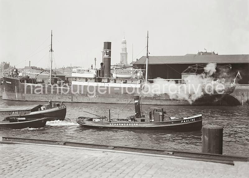 Historische Fotodokumente aus dem Archiv der HHLA - Schiffe im Sandtorhafen / Frachtschiff am Sandtorkai; alte Hamburg Bilder auf Fotoleinwand oder Posterprint.  0117_753a Das Frachtschiff CHORZOW liegt vor dem Schuppen 1 am Sandtorkai des Sandtorhafens. Der Schlepper PAULINE der Fa. Harms & Sohn fhrt in das Hafenbecken mit zwei Schiffen im Schlepp. lIm Hintergrund der Turm der St. Michaelis Kirche.